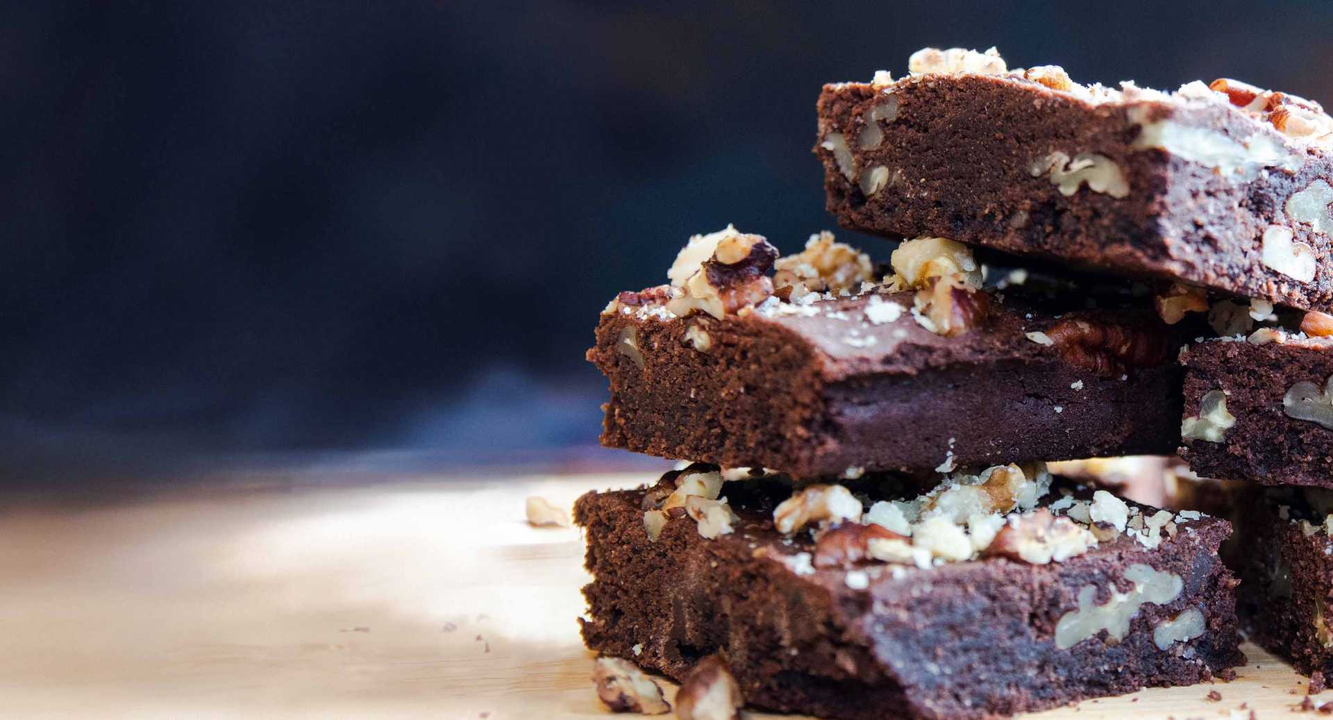 A stack of chocolate and pecan brownies, sprinkled with pecan crumbs and crushed walnut, fresh out of the oven